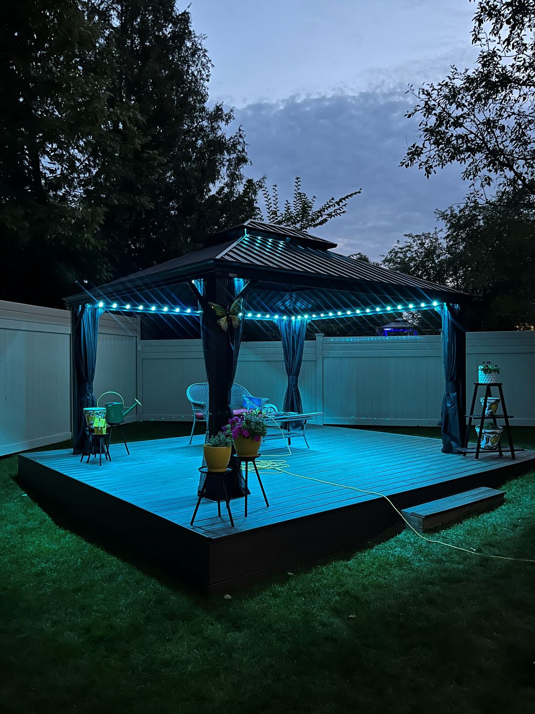 Backyard gazebo on a deck lit with teal permanent lights at dusk