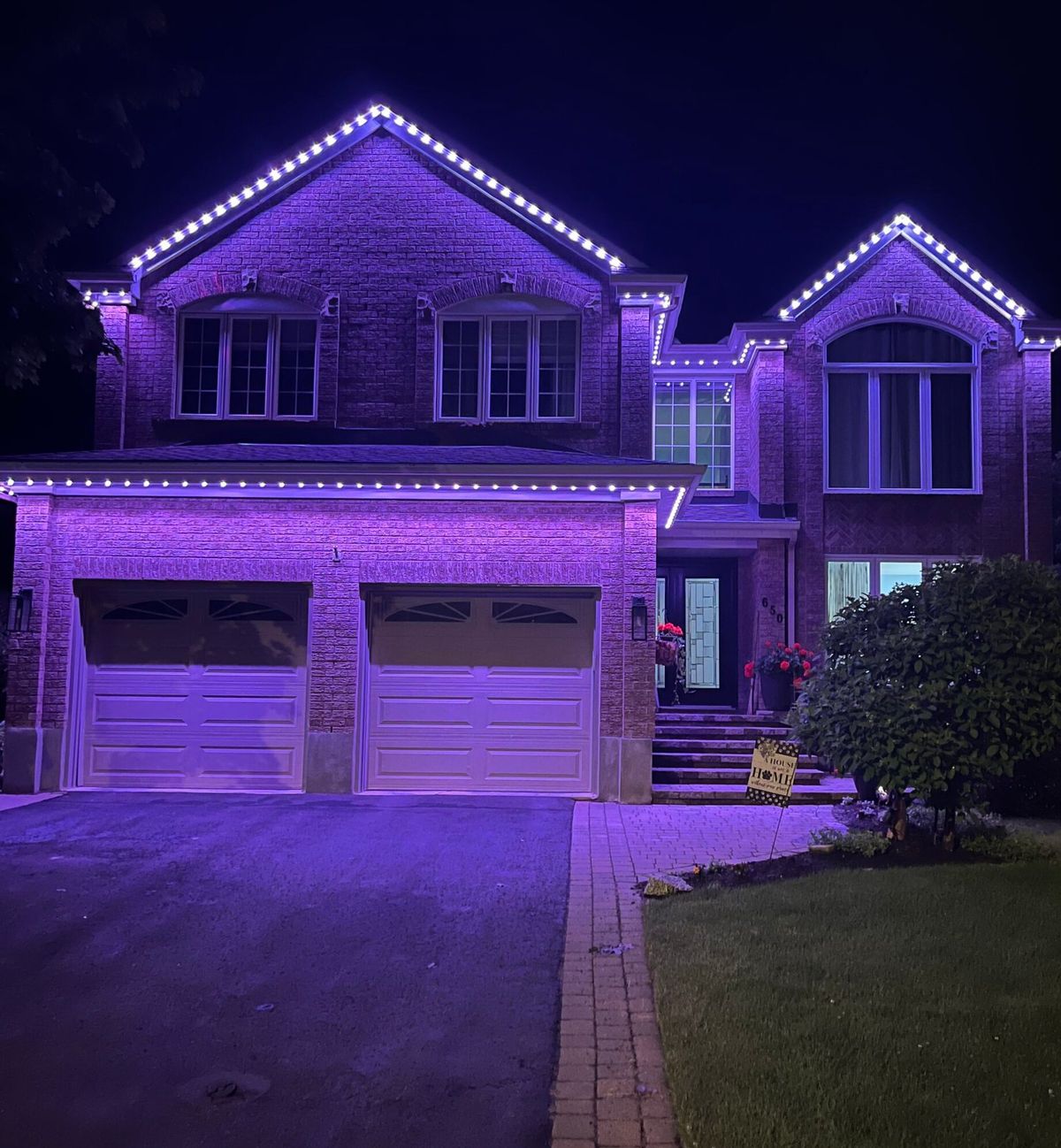 The same home at night with purple permanent lights along both gables and the garage roofline