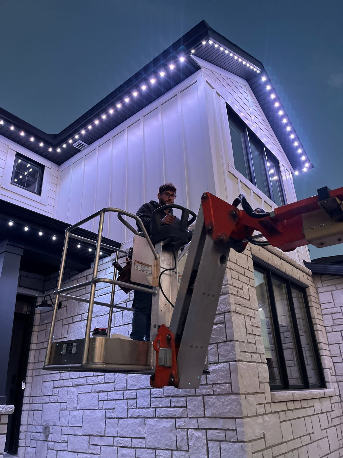 House Homie installer on a lift beside a freshly lit roofline