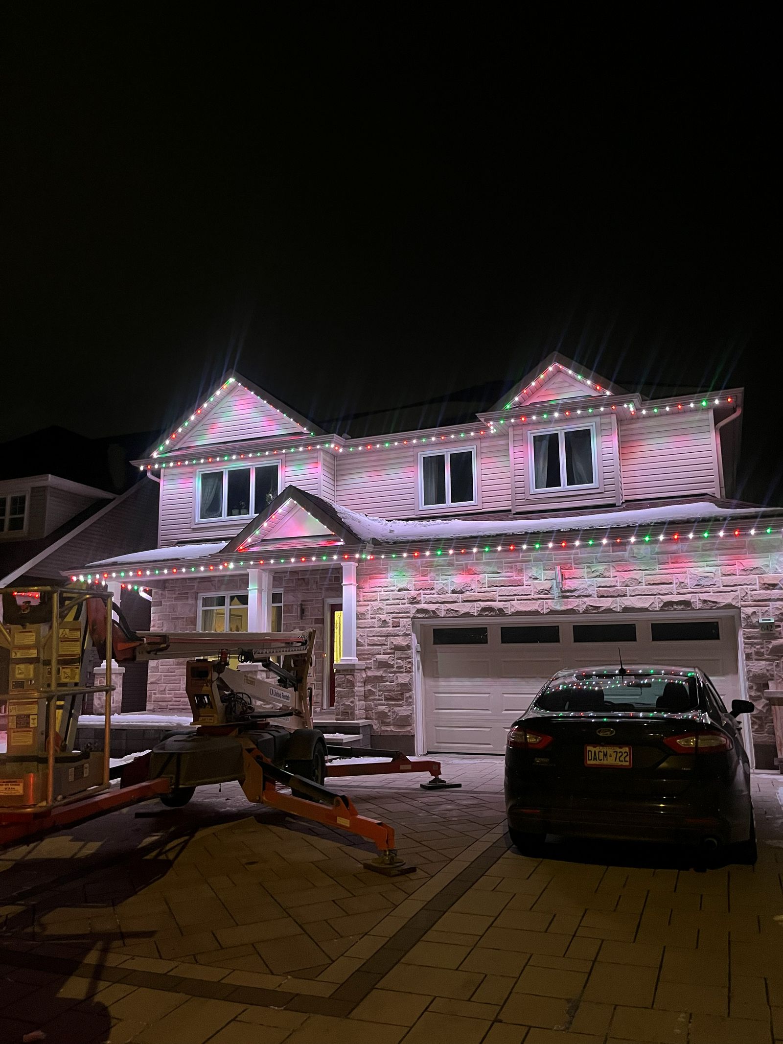 Two-storey home in the snow with red, green and white permanent lights on every roofline